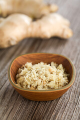 Freshly grated ginger in small bowl with ginger roots in the back (Selective Focus, Focus one third into the image)