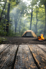 A blurred background of a camping area features tents and a campfire in a forest, with an empty wooden tabletop for product display montage.