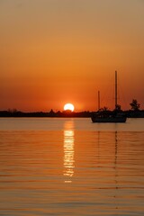 Fototapeta premium Serene sunset over calm waters with silhouetted sailboat.