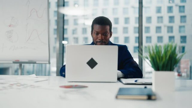 Frontal portrait of financial analyst or CEO Manager in office with laptop. African American male person closing notebook and leaning on chair back, rejoicing by end of working day or good project