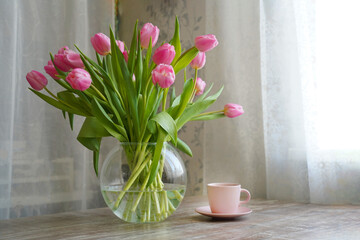 A bouquet of tulips in a round vase on the table and a cup of coffee or tea. Spring Morning Concept