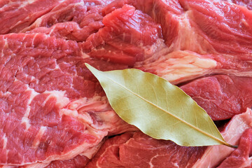Closeup of raw shoulder top blade beef meat steaks to make stew. Red meat background with a single bay leaf from the laurel tree. Top view image