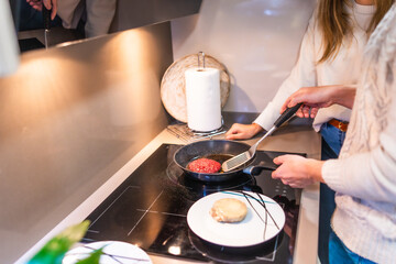 Couple cooking hamburger patties on modern induction stove top