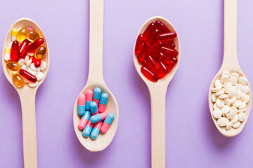 Vitamin capsules in a spoon on a colored background. Pills served as a healthy meal. Red soft gel vitamin supplement capsules on spoon