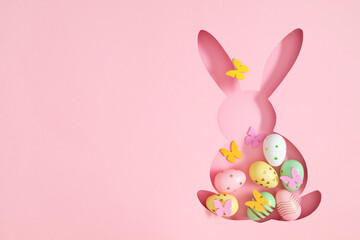 Frame in the shape of Easter bunny filled with colorful Easter eggs on pink background. Top view.