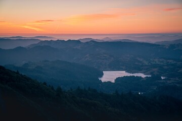 View of rolling hills and a serene lake at sunset, with a vibrant sky in the background