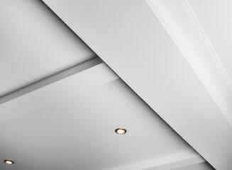 Suspended and grid ceiling with LED spots lamps and drywall construction in empty room in house interior. Stretch ceiling white and complex shape.