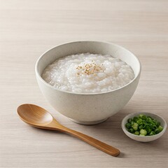 Congee Comfort: A bowl of creamy congee, topped with sesame, is served with a wooden spoon and a side of chopped green onion, capturing the simplicity and warmth of a comforting meal.