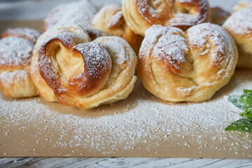 Homemade buns sprinkled with powdered sugar on a wooden background.