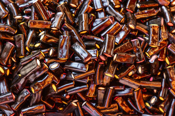 Background of licorice tube shaped candies with a glossy black surface cut edges reveal colorful fillings creating a textured and rich composition