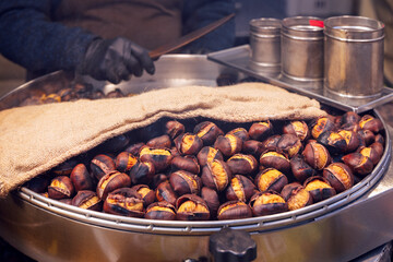 Large metal pan filled with freshly roasted chestnuts golden interiors visible through cracked shells burlap cloth keeps the nuts warm as steam rises