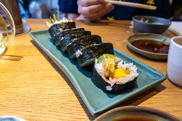 Delicious sushi rolls filled with fresh fish and avocado, sprinkled with sesame seeds and topped with passion fruit, presented on a ceramic plate