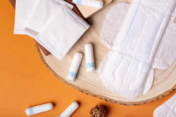 Menstrual hygiene pads and tampons from above on a wooden desk on orange background. Soft cotton...