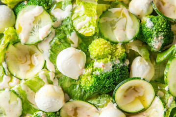 Fresh garden salad with lettuce, cucumbers, broccoli, and mozzarella balls drizzled with creamy dressing, perfect for healthy eating or vegetarian recipes.