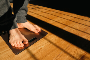 Man measuring her weight using scales on floor on a sunny morning. Man checking his weight on...