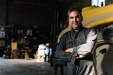 Portrait of smiling farmer with arms crossed in barn workshop with tractor