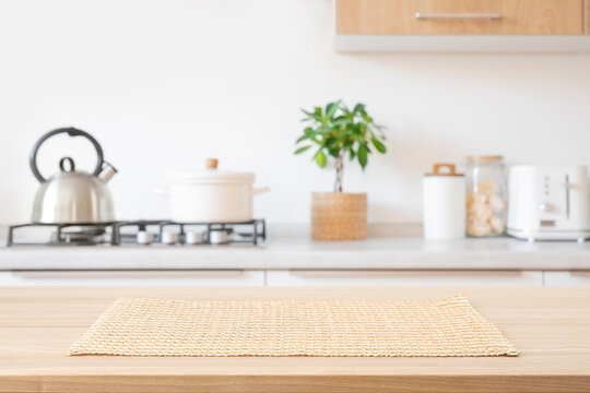 Beige woven rectangular placemat on wooden table top over blurred kitchen room gas stove counter background