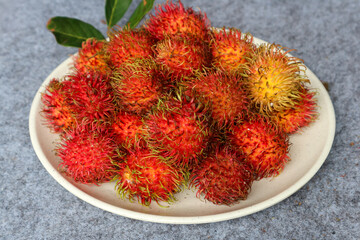 Rambutan fruit in a white plate on gray background