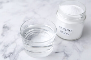 Glass of water and baking soda on white marble table, selective focus