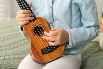 Fototapeta premium Little girl with ukulele on bed at home, closeup