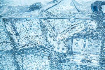 Refreshing soda water with ice cubes as background, closeup