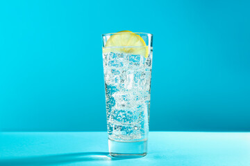 Soda water with lemon and ice cubes in glass on light blue background