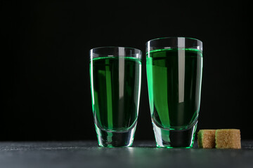 Absinthe in shot glasses and brown sugar on table against black background, space for text
