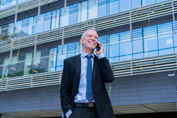 Confident businessman engaging in a phone conversation while smiling and dressed in a professional...