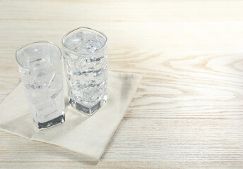 Refreshing soda water with ice cubes in glasses on light wooden table, closeup. Space for text