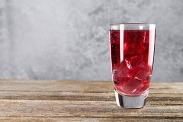 Sweet soda water with ice cubes in glass on wooden table, space for text