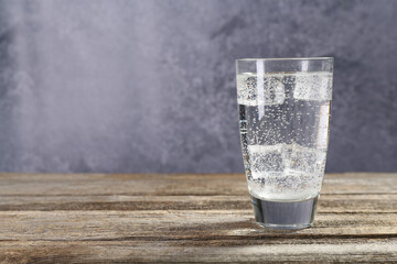 Soda water with ice cubes in glass on wooden table, space for text