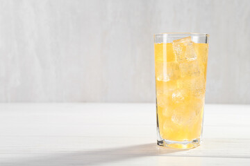 Sweet soda water with ice cubes in glass on white wooden table, space for text