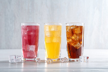 Soda water of different flavors in glasses with ice cubes on white wooden table