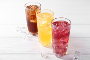 Soda water of different flavors in glasses with ice cubes on white wooden table