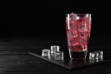 Sweet soda water in glass with ice cubes on black wooden table, space for text