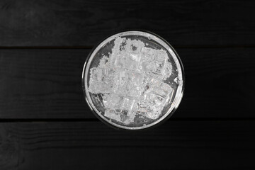 Refreshing soda water with ice cubes in glass on black wooden table, top view