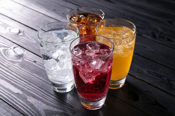 Refreshing soda water of different flavors with ice cubes in glasses on black wooden table
