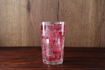 Sweet soda water with ice cubes in glass on wooden table