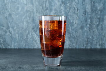Sweet soda water with ice cubes in glass on grey table