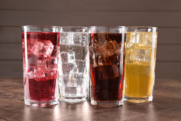 Refreshing soda water of different flavors with ice cubes in glasses on wooden table