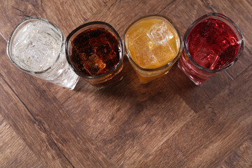 Refreshing soda water of different flavors with ice cubes in glasses on wooden table, flat lay....