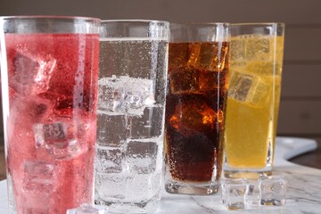 Refreshing soda water of different flavors with ice cubes in glasses on table, closeup
