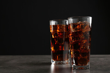 Cold cola with ice cubes in glasses on grey table against black background. Space for text