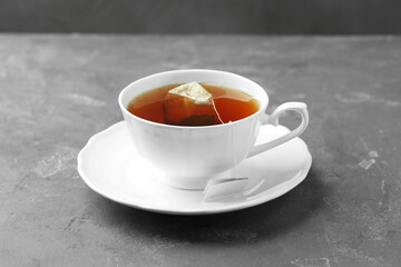 Tea bag in cup with hot drink on gray textured table