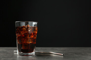 Cold cola with ice cubes in glass and drinking straw on grey table against black background. Space for text