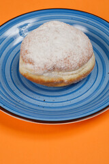 An overhead shot of a single doughnut sprinkled with powdered sugar, placed on a blue plate with a circular pattern, set against an orange background
