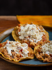 Tostadas with chicken tinga, cheese and cream on a plate on a wooden table. Typical Mexican food