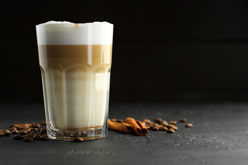Tasty latte macchiato in glass, coffee beans and cinnamon on black table, closeup. Space for text