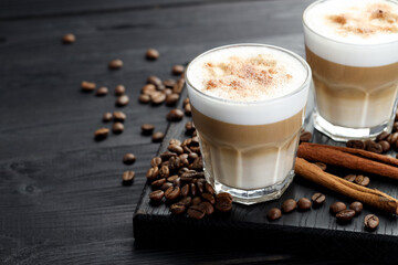 Tasty latte macchiato in glasses, coffee beans and cinnamon on black wooden table, closeup. Space...