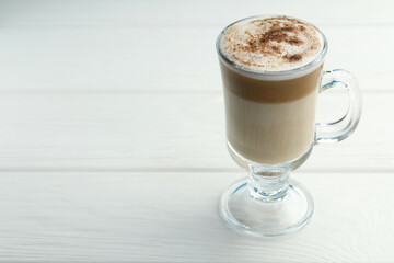 Tasty latte macchiato in glass cup on white wooden table, closeup. Space for text